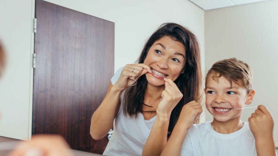 Mother and young son smile in the mirror while flossing teeth. Mother and young son smile in the mirror while flossing teeth.