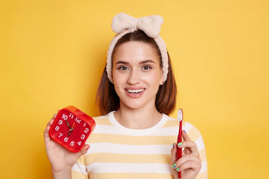 Woman with a pink headband holds a toothbrush and a clock