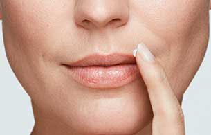 Close up of a woman pointing to a cold sore on her lips. 