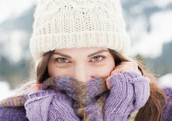 Woman wearing a white winter hat and covering her face with a purple scarf