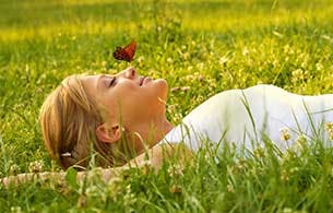Woman lying in a grass field with a butterfly sitting on her nose