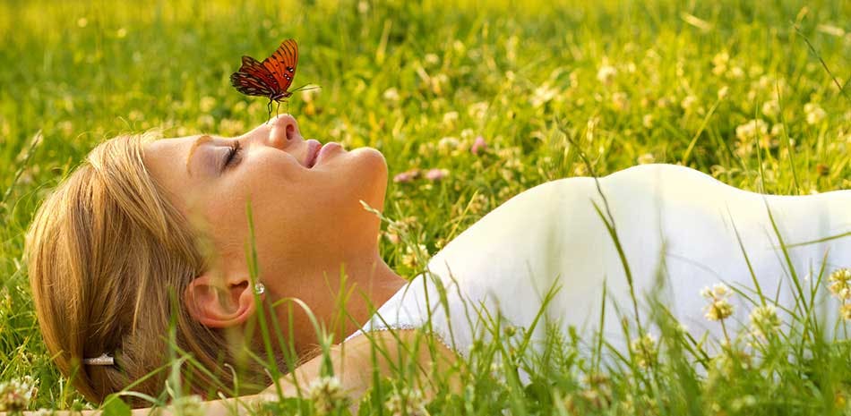 Woman lying in a grass field with a butterfly sitting on her nose