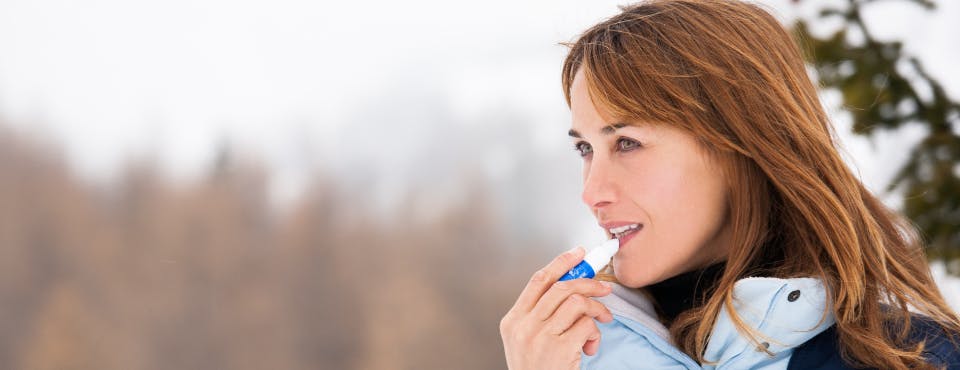 Woman in winter coat putting lip balm on Woman in winter coat putting lip balm on