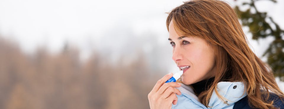 Woman in winter coat putting lip balm on 