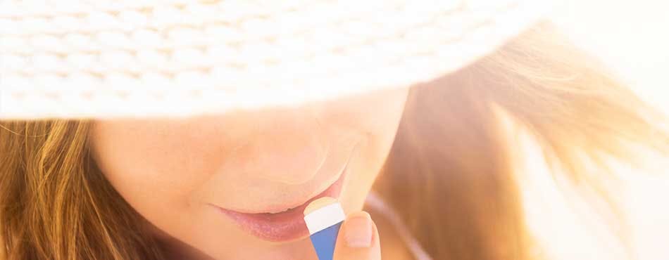 Woman in a sun hat applying lip balm