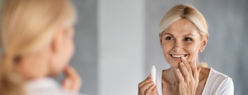 Woman applying lip balm in front of mirror