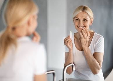 Woman applying lip balm in front of mirror