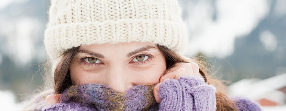 Woman outdoors in a knitted hat holding her scarf over her face 