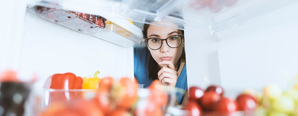 Young woman looking intently at fresh food in fridge