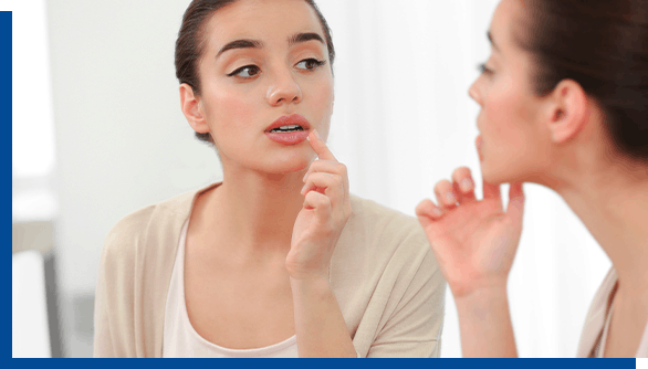 Young woman looking in mirror while applying Abreva Cold Sore Cream