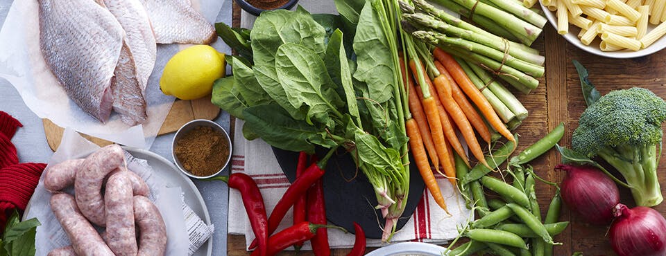 Divers légumes, saucisse et poisson crus disposés sur une table