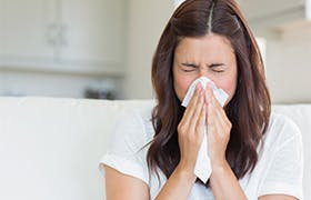 Brunette sneezing in a tissue in the living room