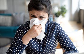 Young woman sneezes into a tissue as she tries to relieve her congested nose.