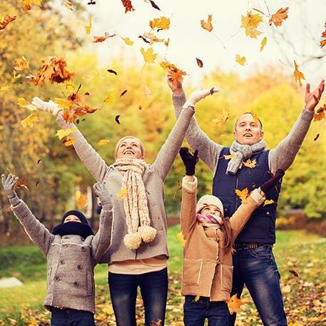 Young family in the forest throwing leaves in the air at the same time during autumn