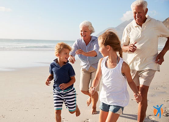 Elderly couple smiling while running on the sandy beach along with their grandkids