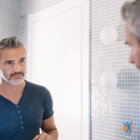 Mann schaut in einen Badezimmerspiegel