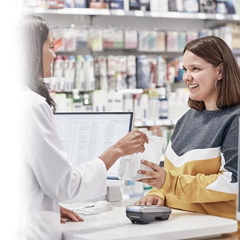 Eine Apothekerin überreicht einer Frau eine Tüte mit Medikamenten in der Apotheke.
