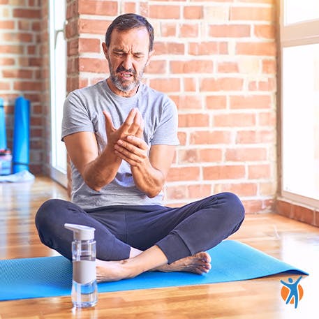 Ein Mann sitzt auf einer Yogamatte und umfasst sein Handgelenk