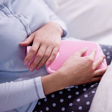 Frau legt rosa Wärmflasche auf den Bauch.