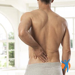 A shirtless man holding his lower back in pain