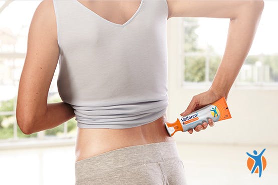 Femme appliquant un gel de soulagement des douleurs musculaires et dorsales Voltaren avec applicateur sur le bas du dos