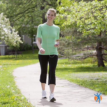 Smiling woman in exercise clothes listening to music as she walks through the park