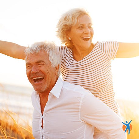 Happy older man giving a woman a piggyback at the beach