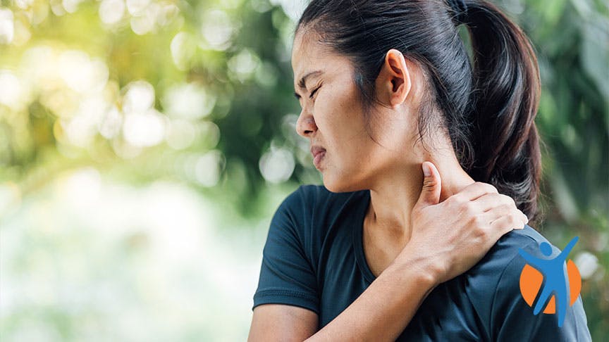 Woman standing in nature and holding her neck in pain Woman standing in nature and holding her neck in pain