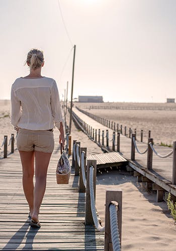 A woman walking along a boardwalk near a beach 