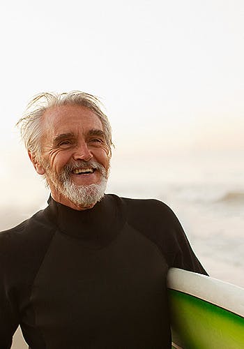 Man smilling while holding his green surf board on the beach