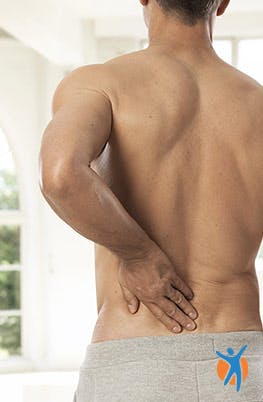 A shirtless man holding his lower back in pain