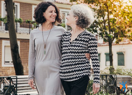 Two women walking arm in arm - reaching out for support to reduce the isolation of pain