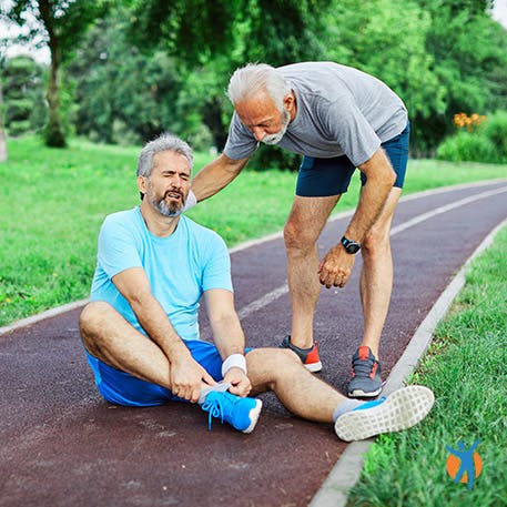 Middle aged man helping friend suffering with acute sprained ankle pain