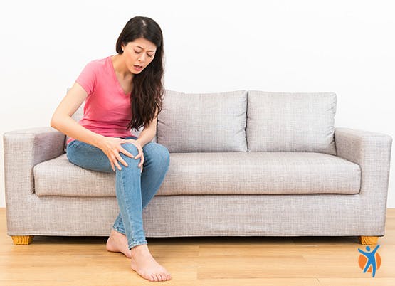 Woman sits on sofa holding knee in pain