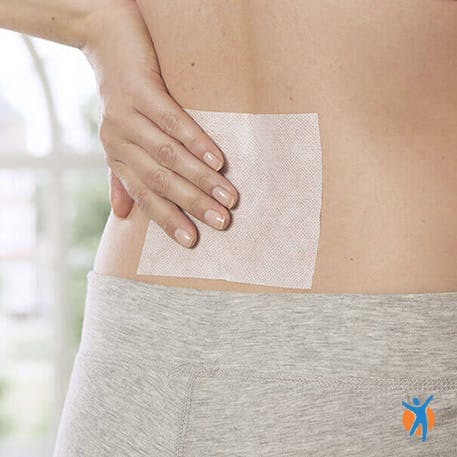 Someone pressing Voltarol heat patch to lower back - learn more about Voltarol Heat Patches