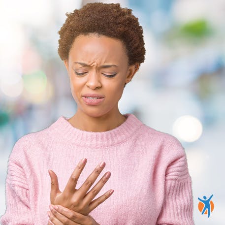 Woman outdoors holding her wrist in discomfort - learn about the symptoms of wrist joint pain