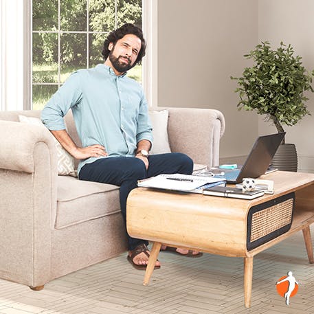 A man working from home holding his lower back in pain while sitting