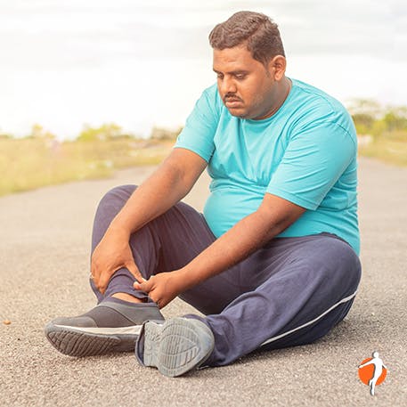 Man siting on pavement worriedly holding his lower leg