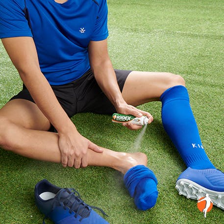 Stretching to help alleviate pain Man spraying his ankle with Iodex UltraGel after a football game