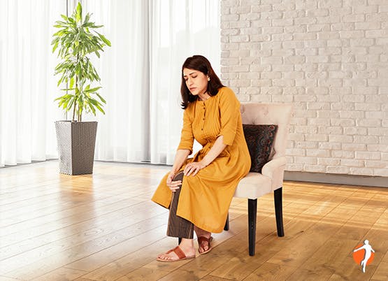 Woman sits on chair holding knee in pain Woman sits on chair holding knee in pain