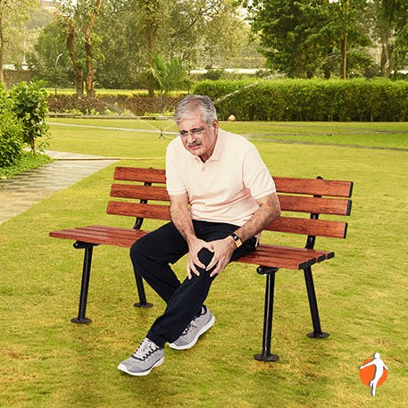 Elderly man holding his knee in pain while sitting on the bench