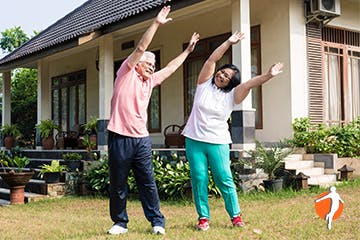 A couple stretching with their arms raised outside their house