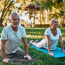 an elderly couple on yoga mats outside stretching their backs