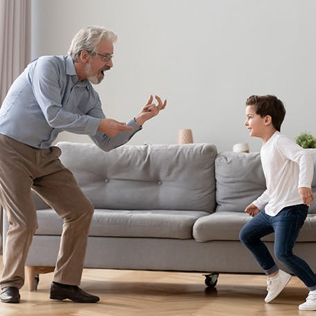 Man dancing with grandson at home, bending knees free from knee pain Man dancing with grandson at home, bending knees free from knee pain
