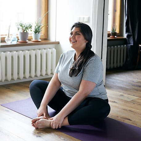 Woman sits on yoga mat at home