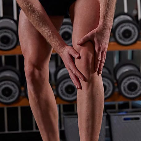 person clutches knee in gym person clutches knee pain in gym