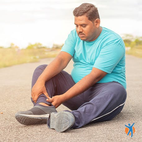 Man sitting on the ground & touching his right feet with both hands