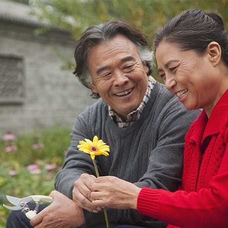 elder middle age man gives his wife a flower in the garden