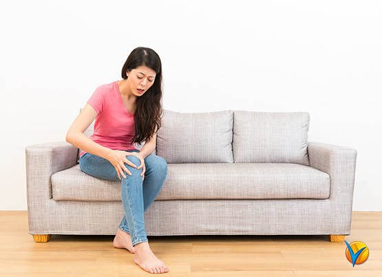 Woman sits on sofa holding knee pain