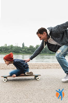 Un homme pousse son fils sur un skateboard.